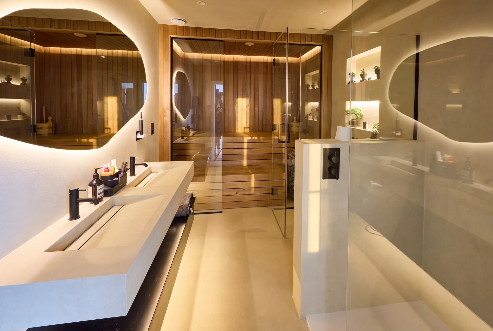 Glass-fronted timber sauna beside sculptural bathroom mirrors