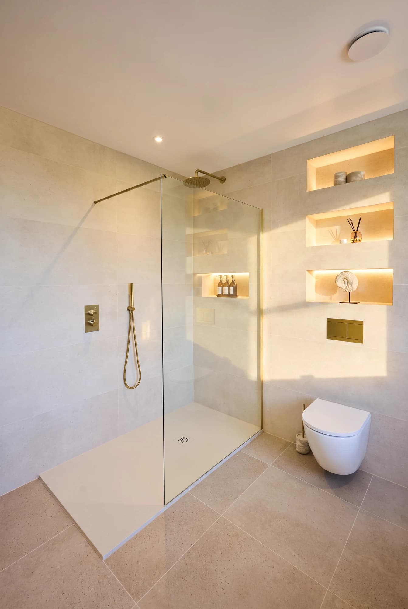 Sunlit shower room with pale stone finishes and illuminated niches