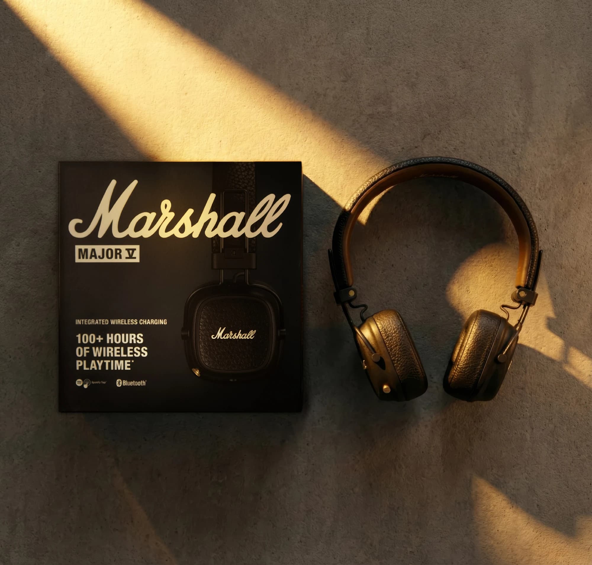 Overhead composition of Marshall headphones and packaging in diagonal sunlight
